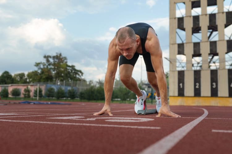 VO₂max-Rechner: Maximale Sauerstoffaufnahme über Cooper-Test, 1-km-Zeit oder Ergometer schätzen Läufer in Startposition auf der Tartanbahn vor einem Ausdauertest
